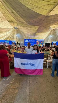 A imagem contêm três professores do Centro de Educação que participaram do CONAE 2024. Da esquerda para a direita está a professora Ozirlei Teresa Marcilino, está com cabelos presos com blusa amarela, o professor Iguatemi Santos Rangel, está com blusa branca e a professora Tatiana de Santana Vieira que está com cabelos soltos e blusa branca. Eles estão segurando a bandeira do estado do espírito santo.